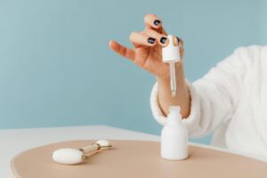 Hand in a bathrobe using a pipette to dispense skincare product into a white bottle.