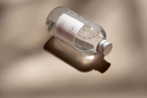 A clear plastic bottle of skincare tonic with bubbles rests on a reflective surface with ample copyspace.