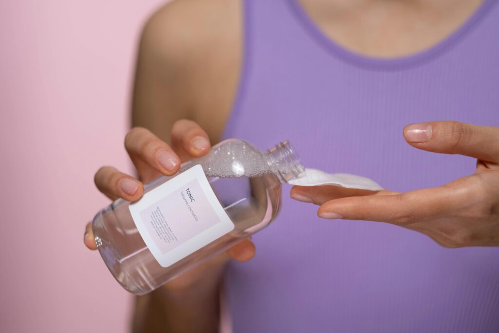 Woman applying skincare tonic with a cotton pad. Focus on hands and product in a studio setting.